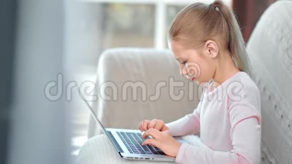 可爱的快乐少女用笔记本电脑坐在沙发上聊天打字视频的预览图