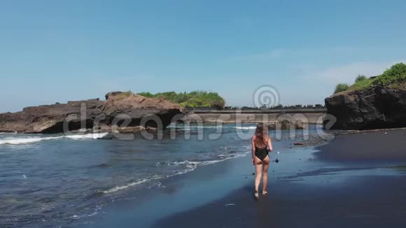 空中无人机后景女性性感屁股穿黑色泳衣走在黑色沙滩上有许多石头和岩石视频的预览图