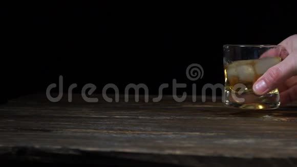手拿一杯黑背景上有冰块的威士忌男人用冰块摇动威士忌玻璃杯视频的预览图