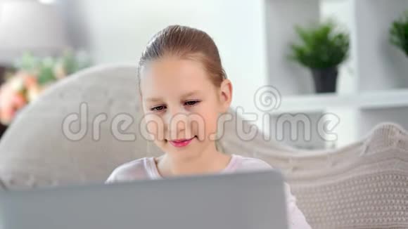 微笑的小可爱的女孩子专注地看着社交网络中的笔记本电脑聊天屏幕视频的预览图