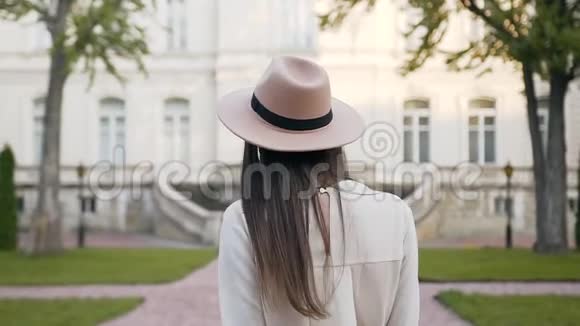 带着长发和时尚帽子的微笑的漂亮女人的后景在走进来的时候她转过身来看着相机视频的预览图