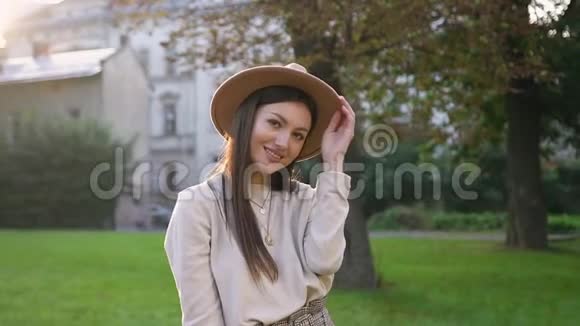漂亮的无忧无虑的快乐女人戴着时髦的帽子在绿树和绿树的背景上真诚地微笑着看着相机视频的预览图