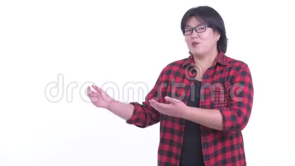 快乐超重的亚洲时髦女人一边说话一边展示视频的预览图