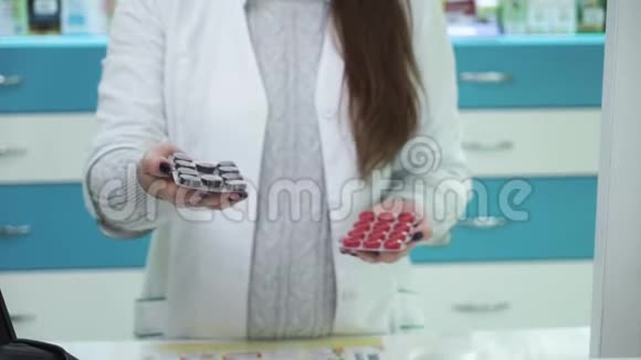 年轻的女药剂师向摄像机显示两种不同的药物黑色和红色药片的选择视频的预览图