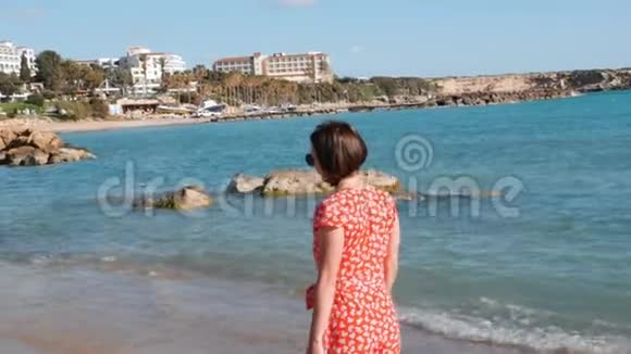 白人黑发女孩走在海边年轻女孩穿着红色连衣裙在沙滩上散步的背面景色吸引人的肖像视频的预览图