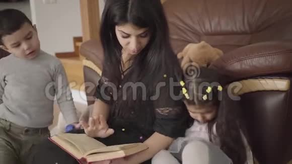 漂亮的中东女人给小孩子读这本书母亲在家教育她可爱的儿子和女儿视频的预览图