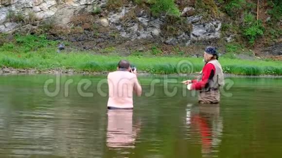 一个留着胡子长发穿着防水服的渔夫正在山河里钓鱼后台专业摄影视频的预览图