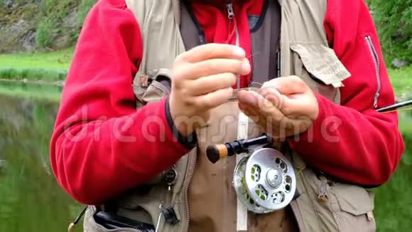 一个钓竿的渔夫把一只苍蝇绑在钩子上用牙齿咬着钓线去钓鱼老人的手视频的预览图