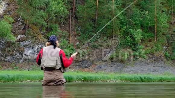 一个穿着防水服的渔夫站在水里手里拿着一根鱼竿一个中年男子正在一座山上钓鱼视频的预览图