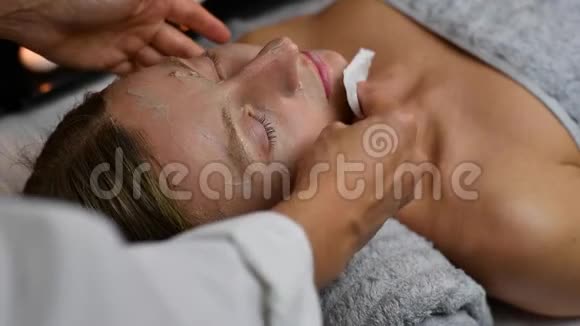 美容师正在去除女性脸上的黏土面具女性在水疗中心接受美容治疗视频的预览图