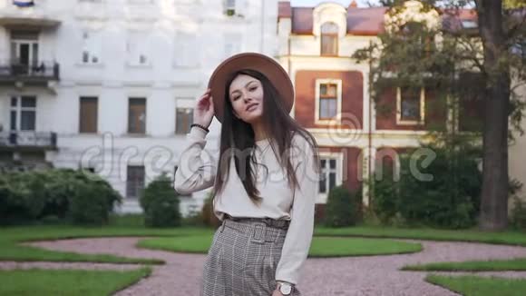 年轻漂亮的30岁女士戴着时髦的帽子在镜头前摆出真诚的微笑在美丽的豪宅前视频的预览图