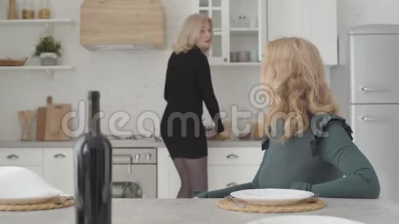 微笑着富有的高加索女人坐在豪华的厨房里拿着一瓶酒说话美丽成熟的女士视频的预览图