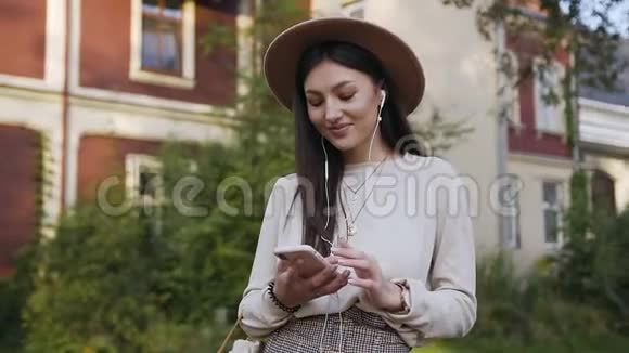 美丽的微笑的幸福女人戴着米色帽子走在美丽的豪宅附近在她的面前寻找美妙的歌曲视频的预览图