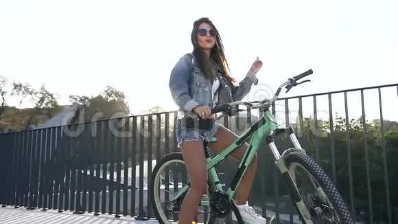 迷人的性感女人穿着诱人的衣服戴着时髦的眼镜坐在自行车上唱歌视频的预览图