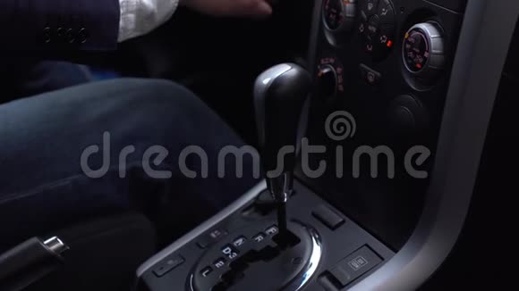 穿着牛仔裤蓝夹克和白衬衫的人把汽车里的自动变速器转移到驾驶上然后降低车速视频的预览图