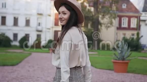 白天在美丽的大厦附近散步时戴着可爱帽子的美丽快乐的女人在镜头前摆姿势视频的预览图