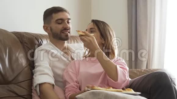 可爱的女人用美味的自制披萨喂她丈夫坐在皮革沙发上幸福的夫妻浪漫视频的预览图