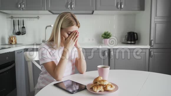 厨房里有药片咖啡和羊角面包的伤心女人视频的预览图