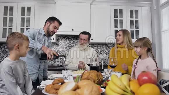 英俊的小胡子把酒倒进酒杯里而他的家人和年长的爷爷坐在一起微笑着快乐视频的预览图