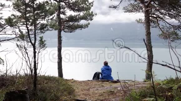 一位年轻的女旅行者坐在挪威峡湾旁视频的预览图