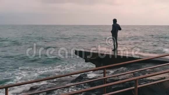 小男孩给暴风雨的大海拍照站在码头拍照的人孤独的男孩拍摄风洋的视频侧视图y视频的预览图