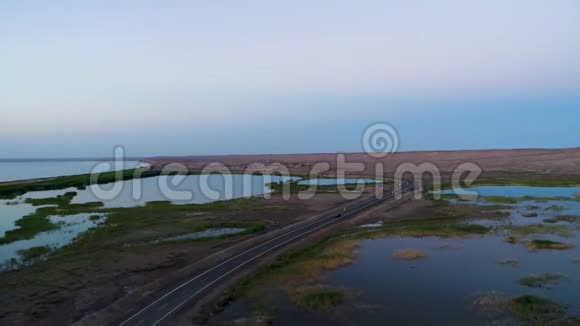 日落时在湖边沙漠的一条空路上驾车的鸟瞰图视频的预览图