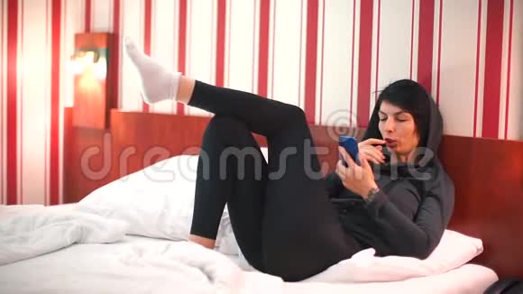 穿外套的女孩在酒店床上使用智能手机视频的预览图