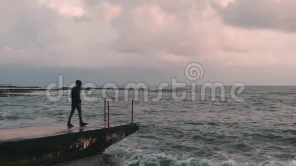 看着暴风雨的海洋的孤独男孩的侧视年轻悲伤的男孩看着地平线忧郁的男孩站在码头年轻的寂寞视频的预览图