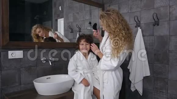 漂亮的金发母亲和她微笑的小儿子在浴室梳头时玩得很开心视频的预览图