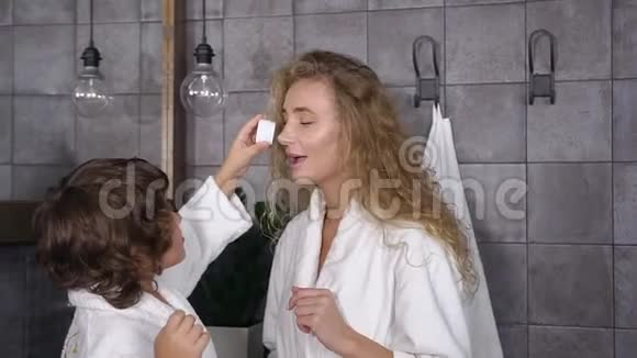 可爱的妈妈和她的儿子在浴室里享受护肤霜的迷人肖像视频的预览图