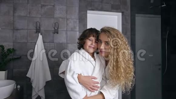 可爱的肖像微笑快乐漂亮的母亲和儿子穿着长袍看着相机视频的预览图