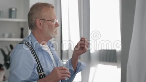 有着灰白胡须的病夫退休后为了健康在靠近窗户的地方吃一粒水感觉更好视频的预览图