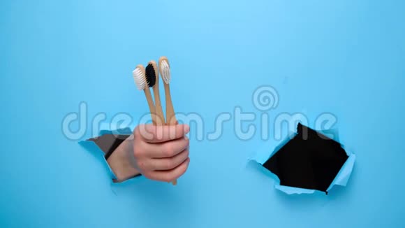 合拢雌性的手做拇指向上的手势演示竹生态牙刷穿过撕裂的蓝色纸墙视频的预览图