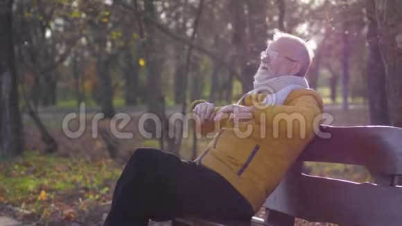 退休后的快乐时光留着灰白胡子的爷爷在公园的长椅上休息享受秋天的时光视频的预览图