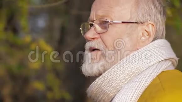 戴眼镜的灰发男子在秋天公园散步的肖像男子脸特写视频的预览图