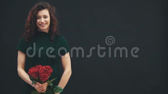 美丽卷曲的黑发女孩闻着红色玫瑰花束与红色条纹的香气视频的预览图
