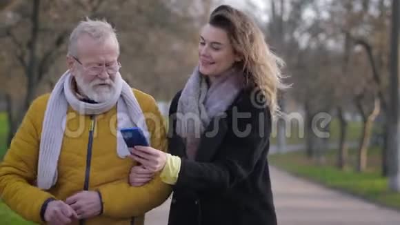 爷爷和孙女在散步时的交流幸福的女孩带着手机向她的老奶奶展示照片视频的预览图