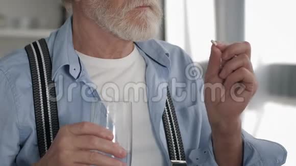 疾病戴眼镜的老人服用药物从玻璃中喝水以促进家庭健康视频的预览图