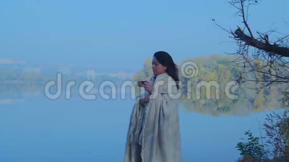 秋高气爽的清晨一个穿着格子花格的漂亮女人手里拿着一杯茶沿着河岸散步视频的预览图