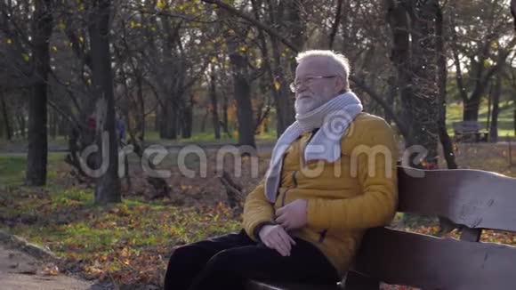 疾病和心脏病戴眼镜的老人在秋天公园的长椅上休息时胸痛视频的预览图