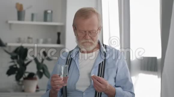 健康和护理戴眼镜的病高年级男子在白色房间里吃药喝玻璃水视频的预览图
