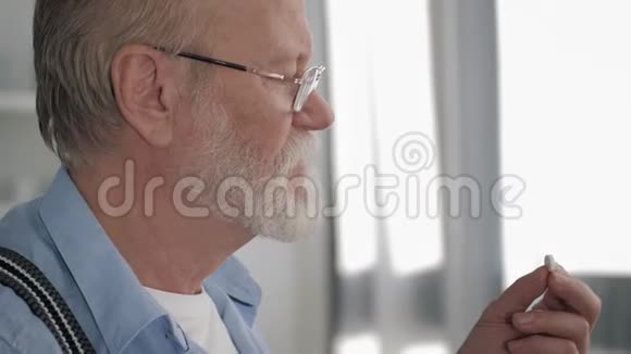 卫生保健一个长着灰胡子的英俊的成熟男人在厨房里吃一粒药丸喝玻璃水视频的预览图