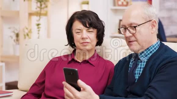 快乐的老年夫妇坐在客厅的沙发上打电话视频的预览图