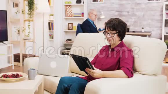 坐在客厅沙发上用平板电脑的老年妇女视频的预览图