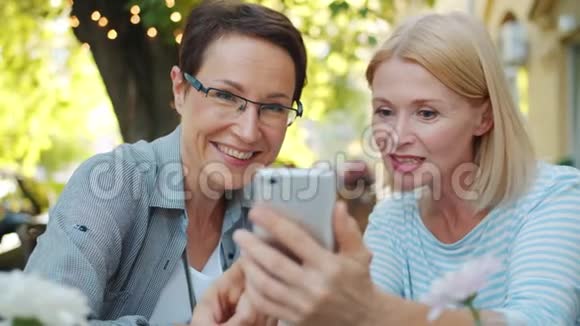 在街边咖啡馆里使用智能手机看屏幕的女性朋友玩得很开心视频的预览图
