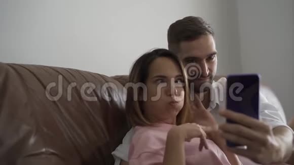 成年夫妇坐在皮革沙发上用手机看照片丈夫和妻子在家休息视频的预览图