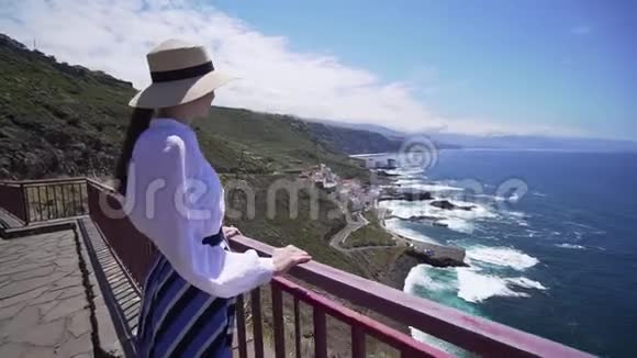 美丽的女孩戴着时髦的帽子在悬崖边上看着大西洋西班牙加那利群岛视频的预览图