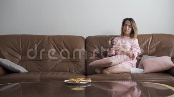 可爱的年轻白种人女人坐在棕色皮革沙发上在家看电视帅哥带着酒瓶视频的预览图