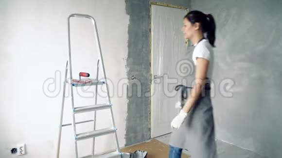 穿着围裙和手套准备粉刷墙壁的年轻女子视频的预览图