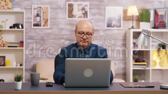 英俊的老人一边喝咖啡一边用笔记本电脑视频的预览图